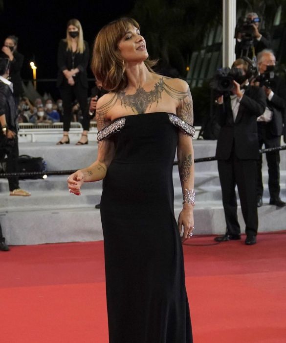 <p>Sul red carpet insieme a papà Dario, per entrambi un look total black, firmato <strong>Givenchy</strong>. L’attrice sfoggia un abito lungo crêpe de chine con spalline gioiello: una scelta da diva che, con un contrasto di gran classe, esalta i tatuaggi su decolleté e spalle di Asia.</p>
