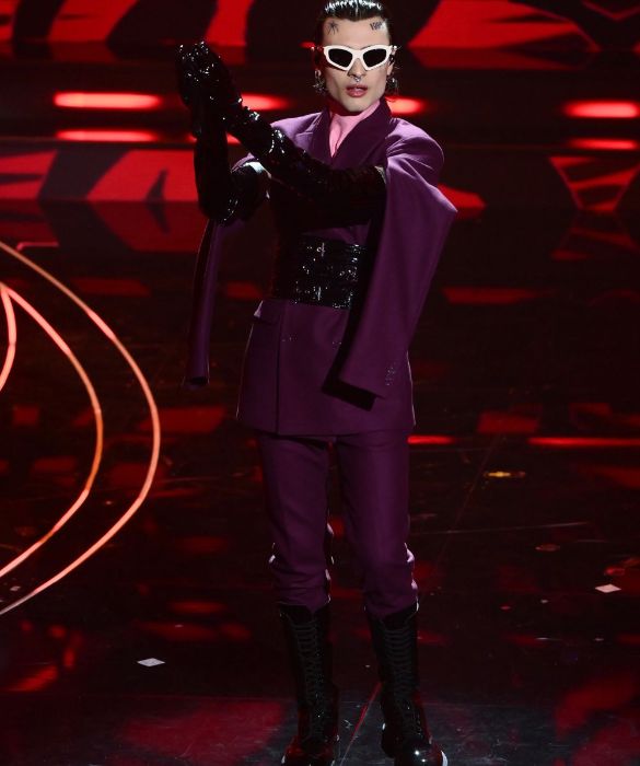 <p>Eleganza <strong>fetish</strong> per l’artista più chiacchieratə del Festival numero 73. Sul palco si esibisce in un <strong>doppiopetto bordeaux</strong> con maniche penzolanti, indossato sopra un <strong>dolcevita in latex rosa</strong> e strizzato in vita da una cintura corsetto. Gli accessori non sono da meno: occhiali da sole sagomati, lunghi guanti di vernice nera e combat boots stringati.</p>