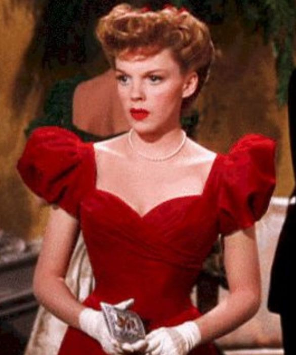 <p>Dopo le scarpette rosse (ne <em>Il mago di Oz</em>, naturalmente) il <strong>vestito rosso</strong>. Infatti, vi viene in mente qualcosa di più natalizio di un abito rosso? Quello di <strong>Judy Garland</strong> in uno dei più grandi classici film di Natale è di una magnifica tonalità di rosso acceso, ha lo <strong>scollo a cuore</strong> incrociato e le <strong>maniche a sbuffo</strong>. A dare quel tocco in più, un filo di perle, il rossetto rosso in tinta con l’abito e un paio di guanti bianchi: il massimo dell’eleganza, per chi si sente perdutamente innamorata della magia del Natale.</p>
