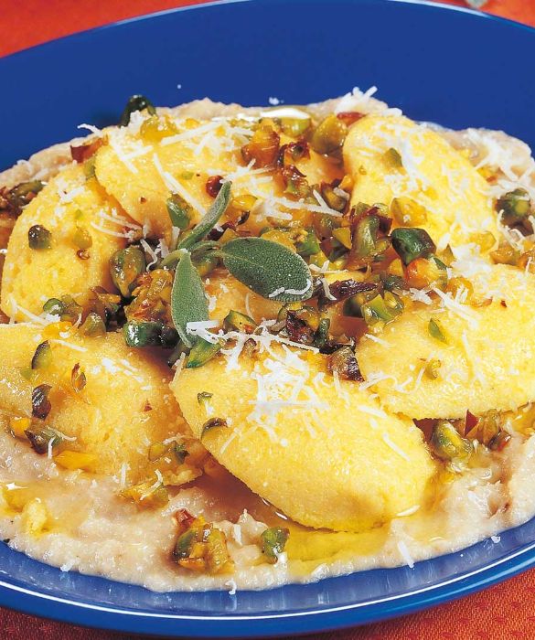 Con l'avvicinarsi dell'autunno la polenta torna di 'stagione'. Ma l'avete mai assaggiata con topinambur e pistacchi? Se volete cucinare questa appetitosa ricetta, preparate la polenta con 350 g di farina di mais, 1,25 l di latte e sale q.b. Nel frattempo, pelate 500 g di topinambur e lessateli in acqua bollente salata per 20-25 minuti. Sgocciolateli e passateli al mixer con 20 g di burro, 2 cucchiai di panna, sale e pepe. Scottate 40 g di pistacchi sgusciati in un pentolino con acqua bollente e privateli della pellicina. Fate appassire un ciuffo di salvia in una padella con 40 g di burro a fuoco basso, unite i pistacchi, salate e pepate. Distribuite la salsa calda sui piatti individuali, poi appoggiatevi sopra la polenta a cucchiaiate. Condite con il burro fuso alla salvia e pistacchi, cospargete con il parmigiano e servite in tavola.