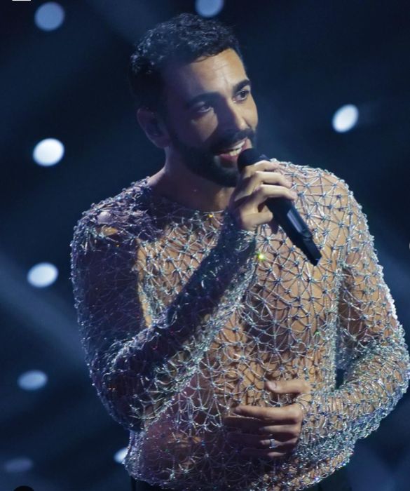 <p>E la sua <strong>maglia metallica</strong>, proprio come dice la canzone <em>Due Vite</em>, il successo con cui ha vinto a Sanremo 2023. Marco Mengoni torna in <strong>Versace</strong> (squadra che vince non si cambia) in una veste nuova, quella di co-conduttore, dalle inaspettate doti di intrattenitore d'insospettabile freschezza. Sul palco si presenta con due completi in pelle, tra cui un tailleur con gonna deliziosamente <strong>gender fluid</strong>, ma il nostro look preferito è quello che lo fa brillare di più. E il due pezzi composto da <strong>maglia-gioiello traforata con cristalli</strong> e pantalone sartoriale lo fa decisamente risplendere nel firmamento sanremese.</p>
